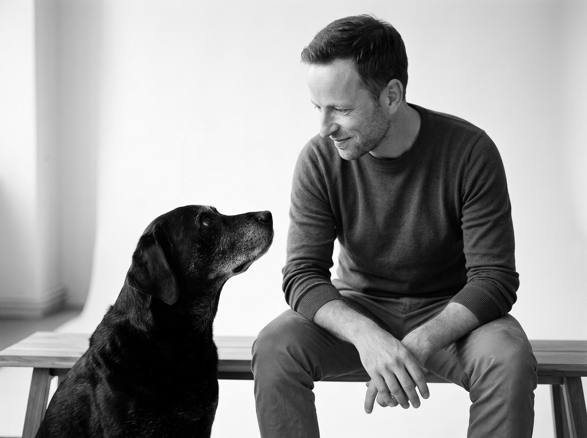Markus sitzt auf einer Holzbank und schaut seinen Labrador Diego an, der zu ihm aufblickt